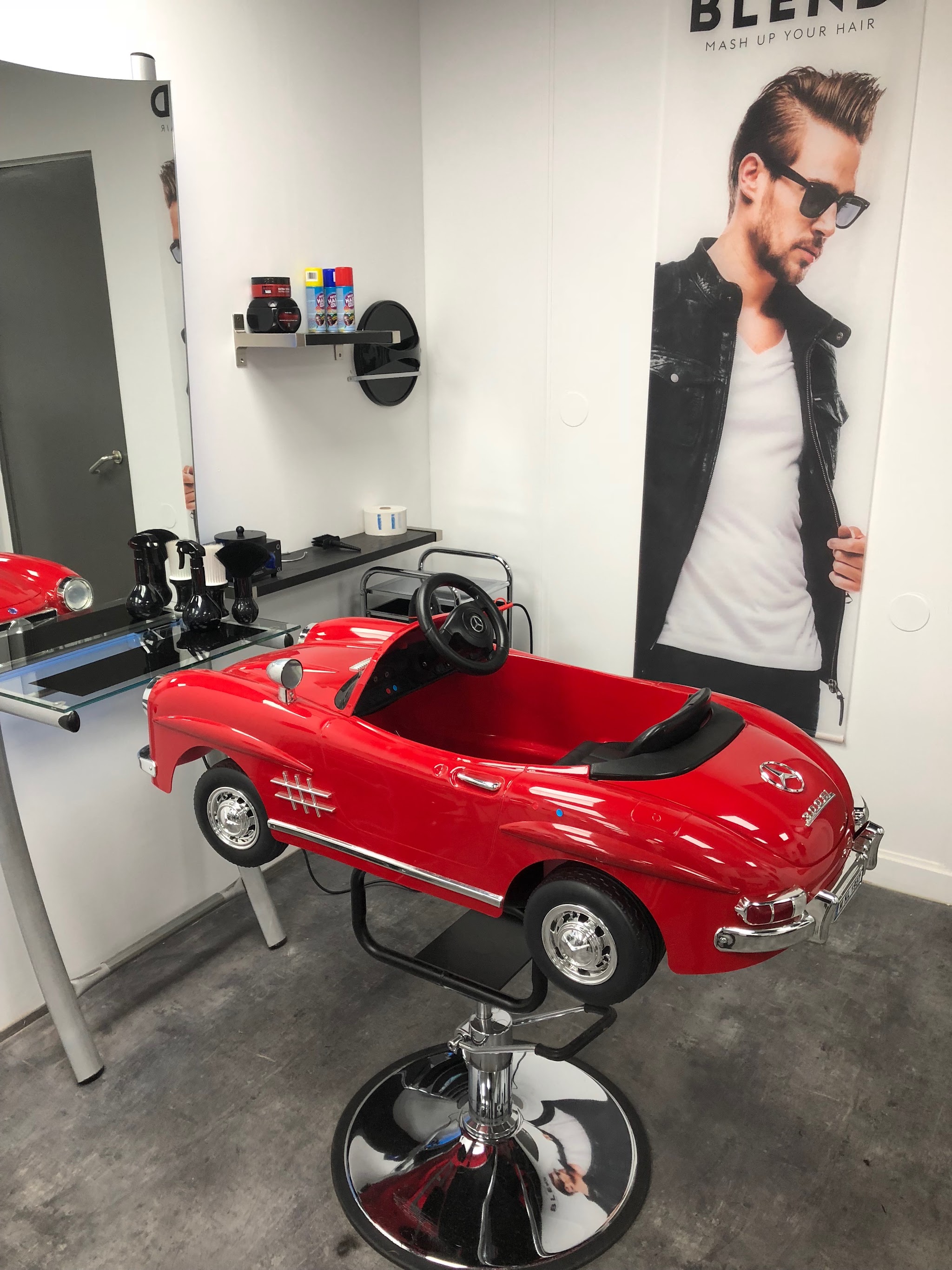 De rode Mercedes trapauto die bij Damas Style als kinderstoel op een kappersvoet staat